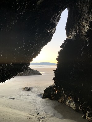 A beach scene with a cave opening to the sea, sandy beach, and distant mountains. - Stinson Beach Cottage - 1 Minute Walk to Beach, in Town with Amenities Galore! (Stinson Beach)