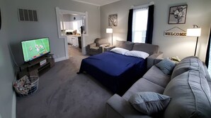 A modern hotel room with a bed, a sofa, a TV, and a kitchenette in the background. - Home Away From Home

 (Warrensburg)