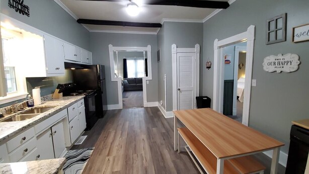 A kitchen with a wooden floor, white cabinets, a black refrigerator, and a wooden bench. - Home Away From Home

 (Warrensburg)