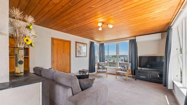 A modern living room with a wooden ceiling, a grey sofa, a TV, and a view of the sea. - Town Gem with Wi-Fi Taupō, large back yard to run around, short 10 min. stroll to town and lake . (Taupō)