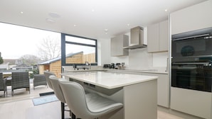 A modern kitchen with a large island, bar stools, and built-in appliances. - Sailors (Falmouth)