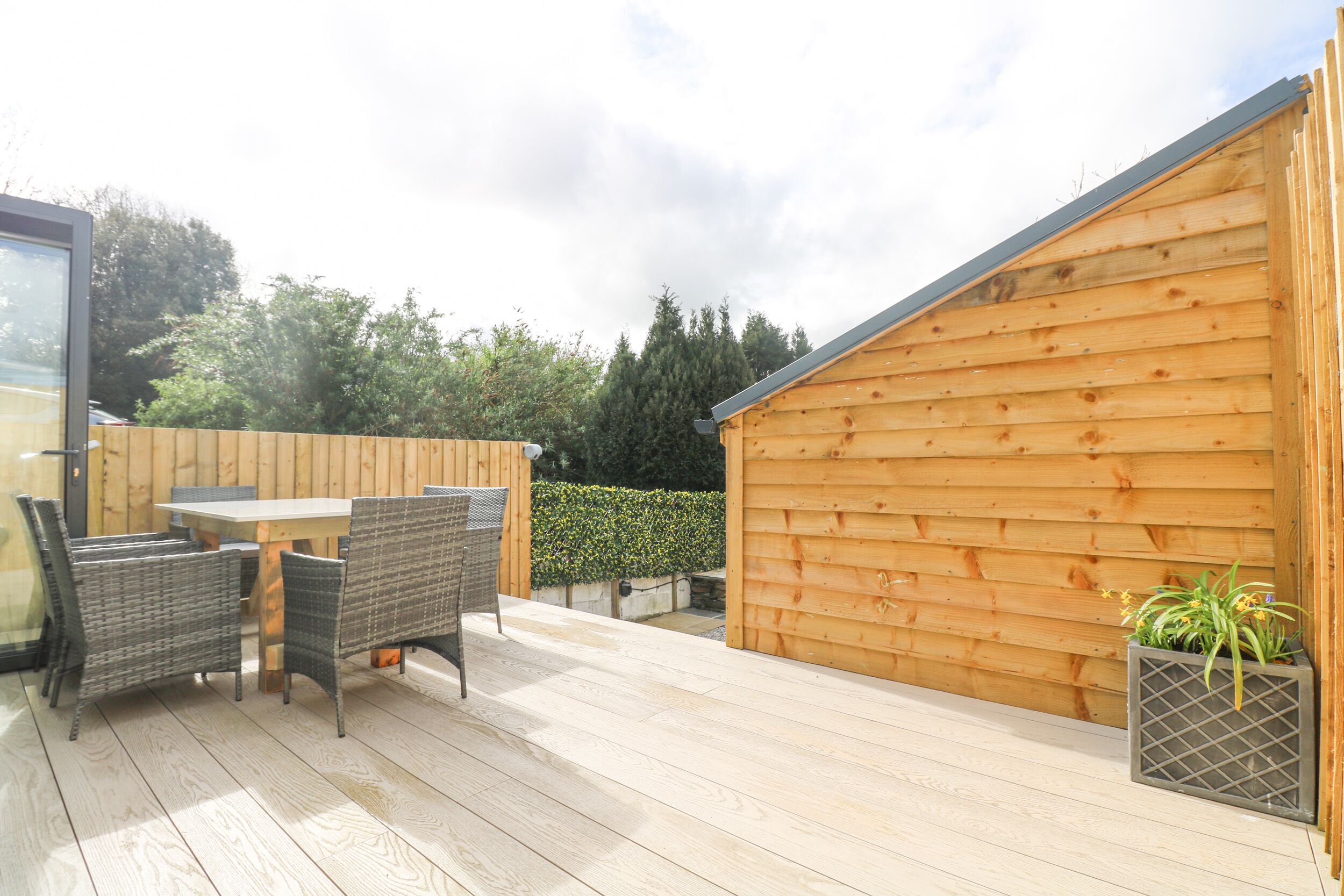 Une terrasse en bois avec une table et des chaises, un abri de jardin en bois et une jardinière avec des plantes.