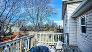 A deck with a round table and two chairs, overlooking a backyard with a wooden fence and trees.