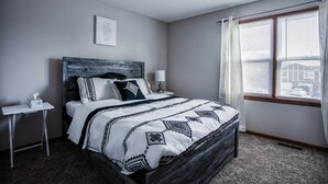 A bedroom with a bed, bedside tables, a window with curtains, and a wall-mounted picture.