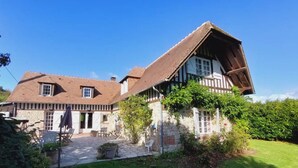 Tipica casa a graticcio con fondamenta in pietra, tetto spiovente e piccolo giardino con prato e piante in vaso.