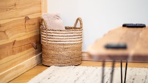 A wicker basket with a cushion on a wooden floor next to a wooden wall. - Lift Haus - New Trailside 2br Condo at Attitash - Clean • Modern • Easy (Bartlett)