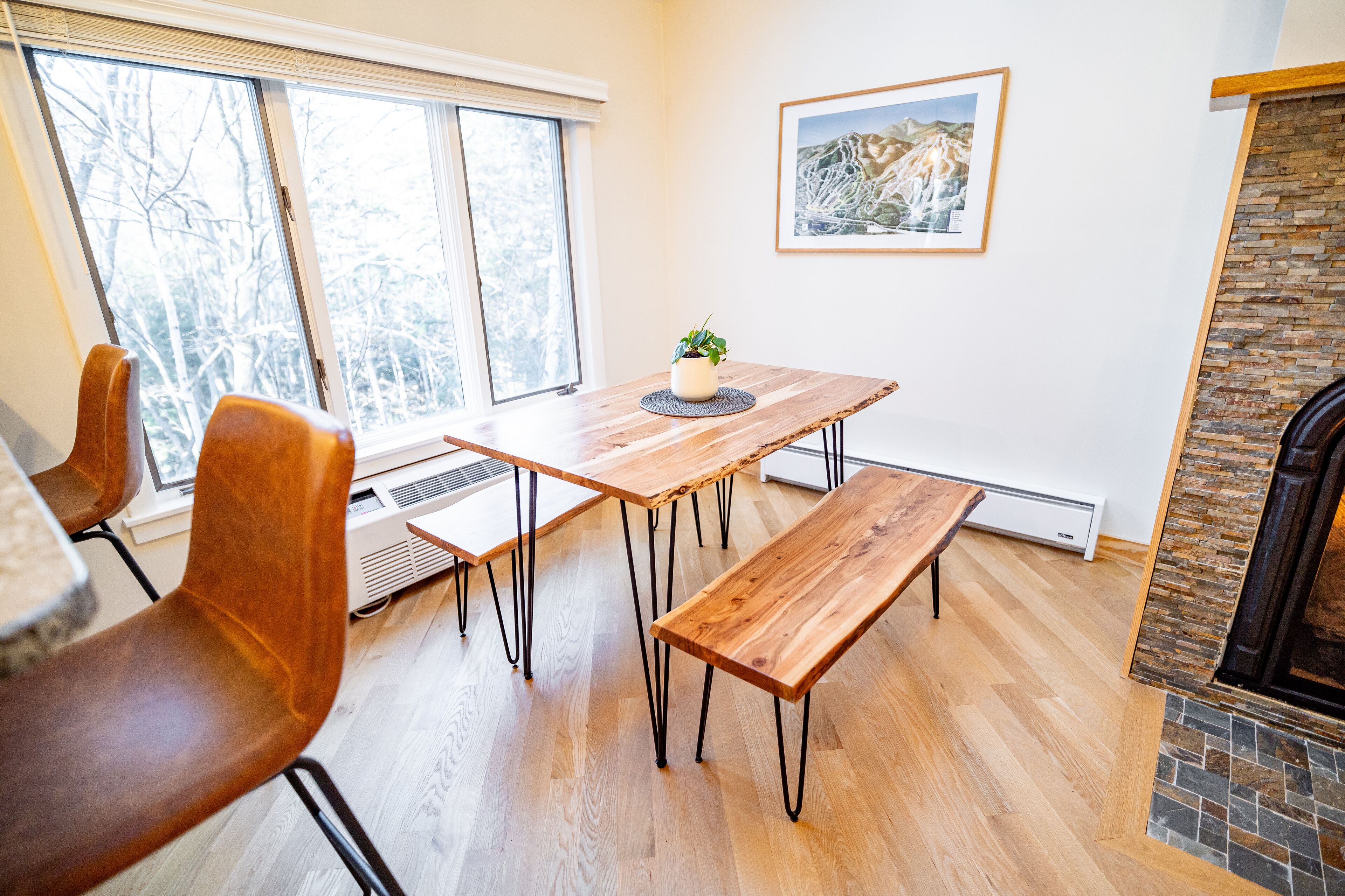 A dining area with a wooden table and benches, a potted plant, and a fireplace.
