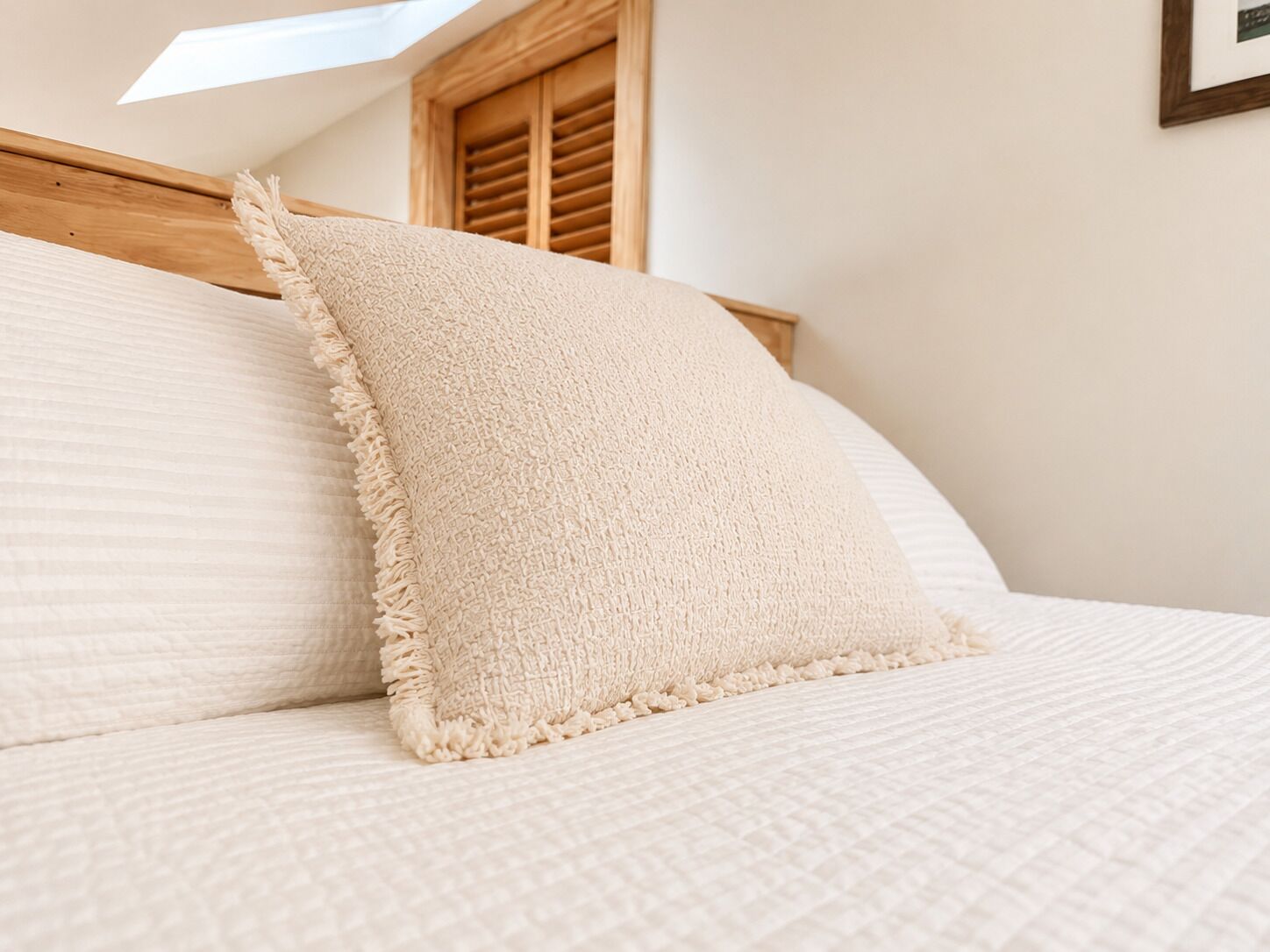 A bed with a textured blanket and pillows, a wooden headboard, and a skylight above.