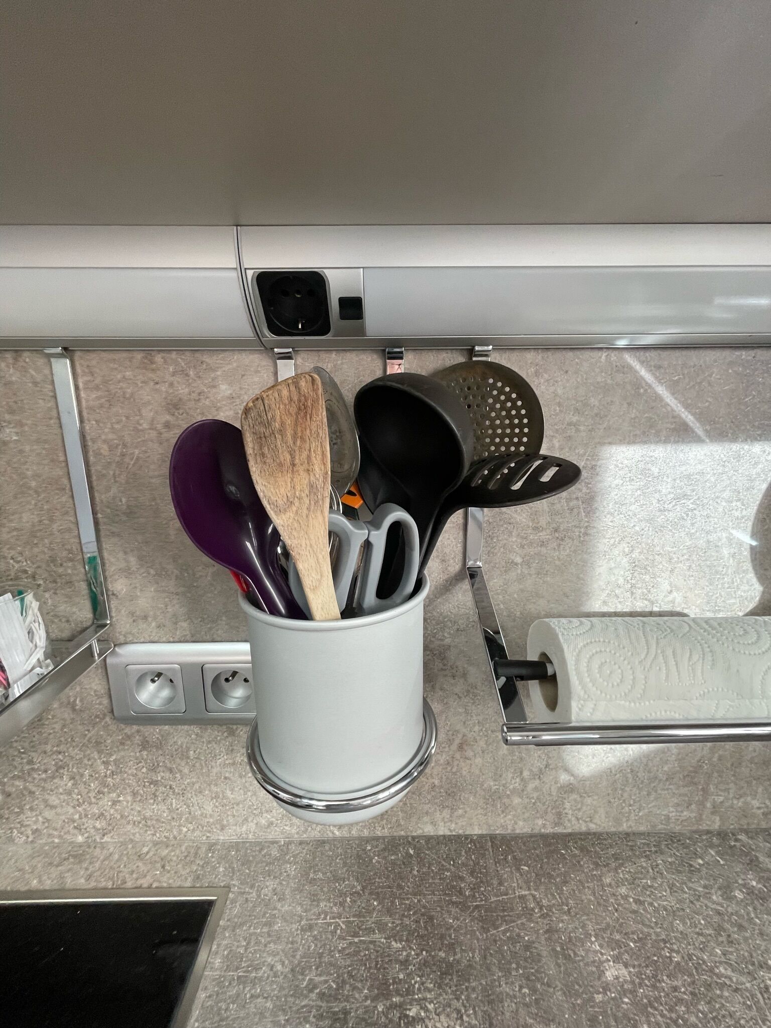 A kitchen with a utensil holder containing a wooden spoon, a purple spatula, and a black spatula.