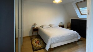 A bedroom with a bed, a nightstand, a lamp, a dresser, and a skylight.