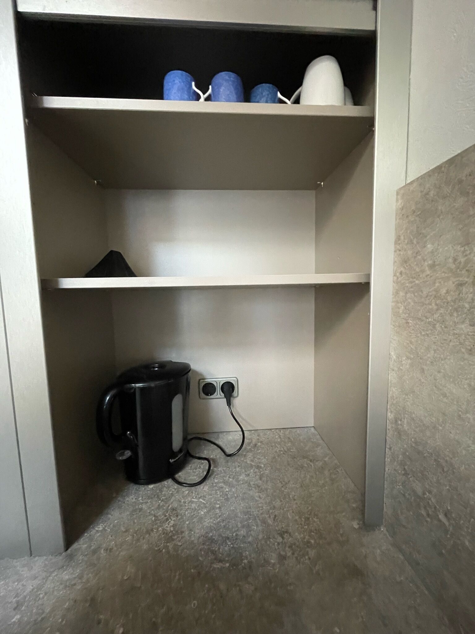 A small, enclosed utility space with a kettle and a power outlet.