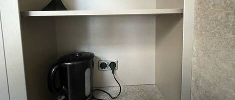 A small, enclosed utility space with a kettle and a power outlet.