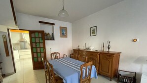 A dining area with a table set for four, wooden chairs, a cabinet with decorative items, and a kitchen in the background.