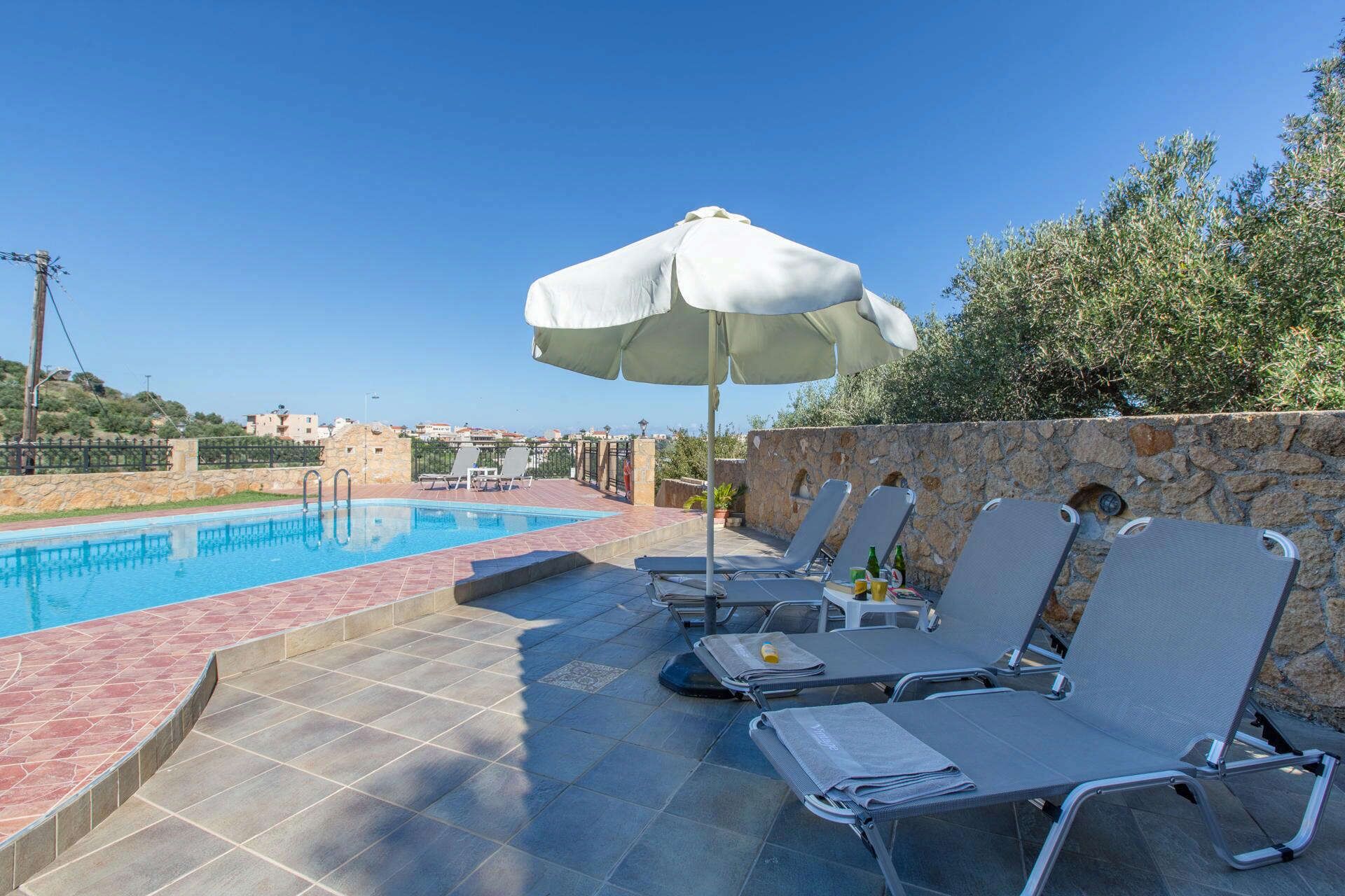 A swimming pool with lounge chairs and an umbrella, surrounded by stone walls and greenery.