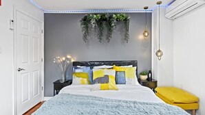 A modern bedroom with a bed, bedside tables, a hanging plant, and a yellow bench. - Brand New Modern Home /w Rooftop Downtown Skyview (Philadelphia)