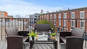 A balcony with wicker furniture, a glass table, and potted plants. - Brand New Modern Home /w Rooftop Downtown Skyview (Philadelphia)