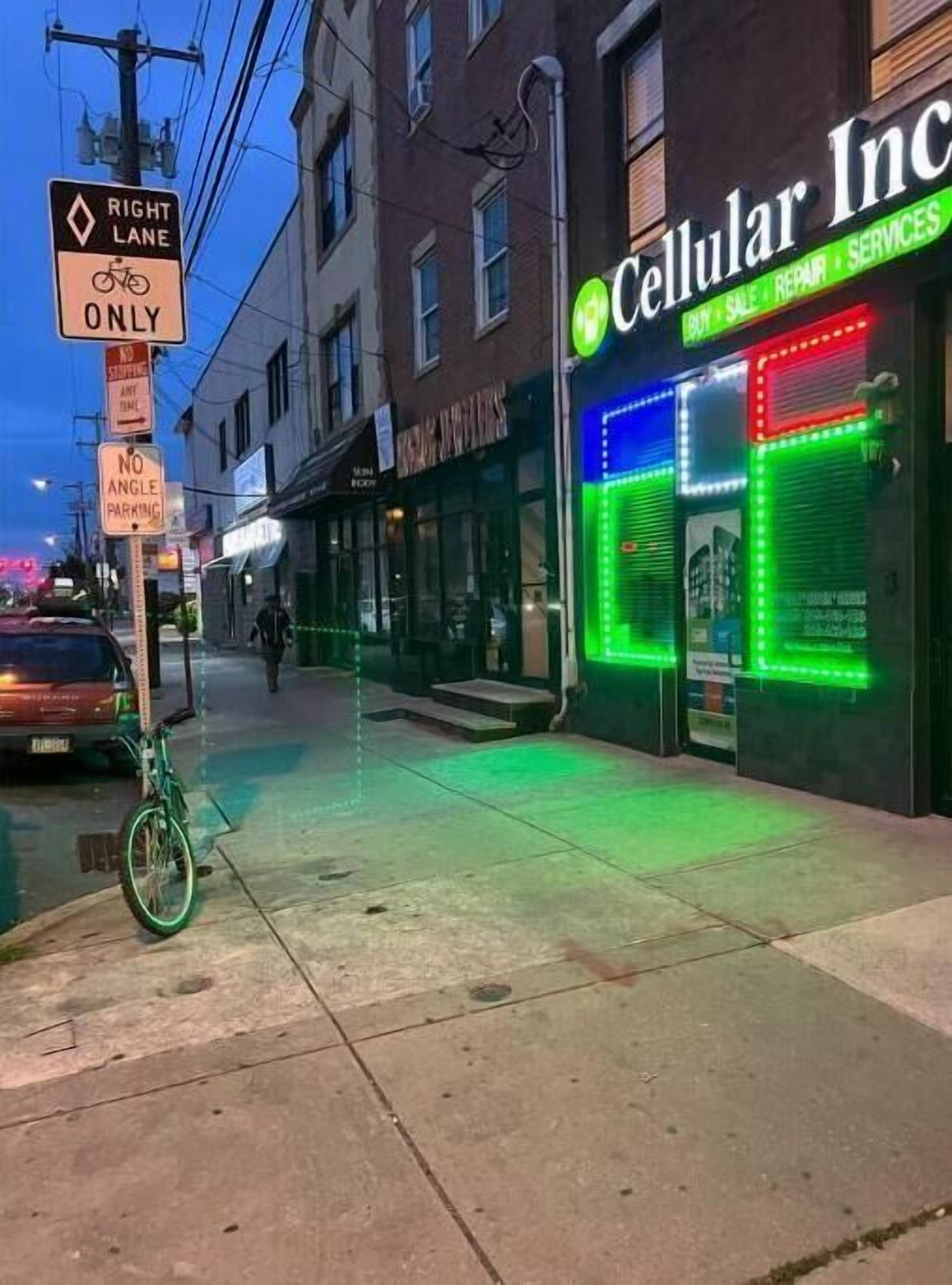A street with a sign indicating a right lane for bicycles only, a no angle parking sign, and a brightly lit storefront with neon lights advertising cellular services.