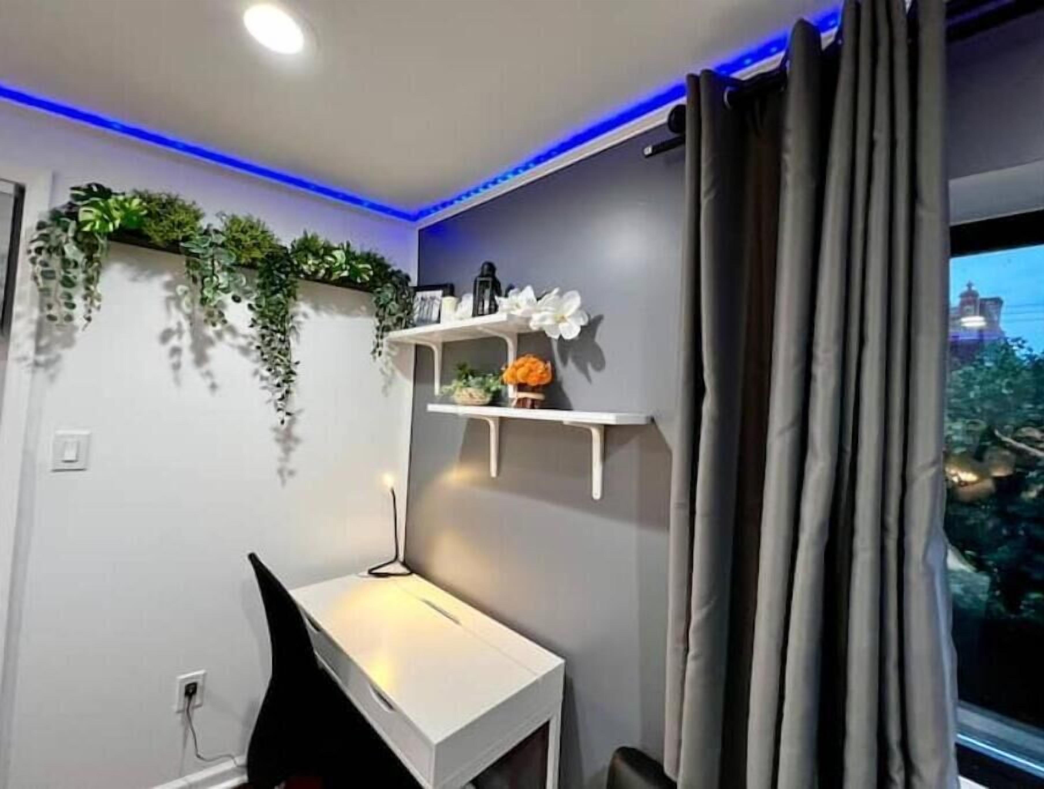 A modern room with a white desk, shelves with decorative items, and a view of a cityscape through the window.