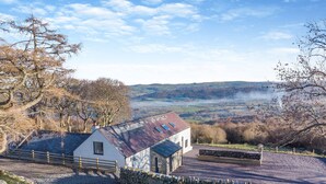 A stone-walled property with a white building featuring a sloped roof, set against a backdrop of hills and a clear sky. - Ysgubor Maen Y Bardd (Conwy)