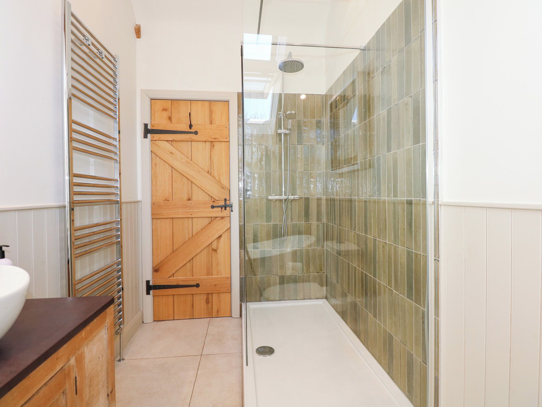 Un bagno con cabina doccia in vetro, porta in legno e lavandino bianco.