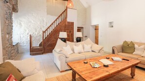 A spacious living room with a wooden staircase, two sofas, a coffee table, and a stone wall. - Ysgubor Maen Y Bardd (Conwy)