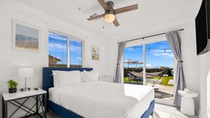 A bedroom with a large bed, a ceiling fan, a window with blinds, and a view of the outdoors. - Salida Del Sol by Rather Be Properties (Desert Hot Springs)