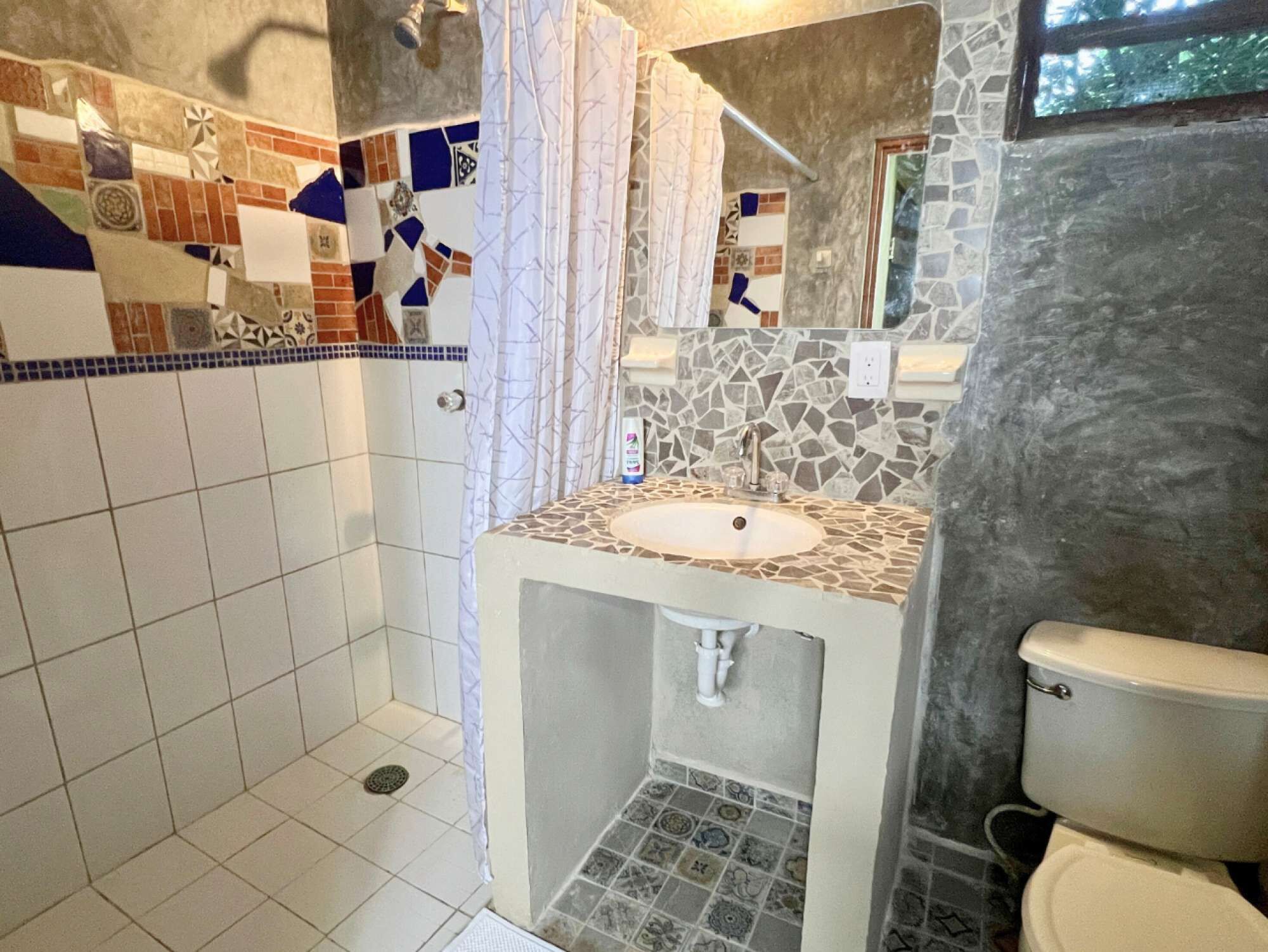 Un baño con ducha, lavamanos e inodoro. La ducha tiene una cortina y el lavamanos está sobre una encimera de piedra.