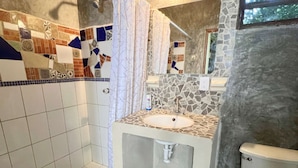 A bathroom with a shower, a sink, and a toilet. The shower has a curtain, and the sink is on a stone countertop. - #8 Tren Maya - Deluxe Family Room (Puerto Morelos)