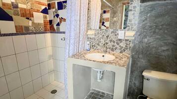 Un baño con ducha, lavamanos e inodoro. La ducha tiene una cortina y el lavamanos está sobre una encimera de piedra.