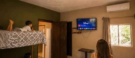 Una habitación con literas, un televisor, un aire acondicionado y una ventana.