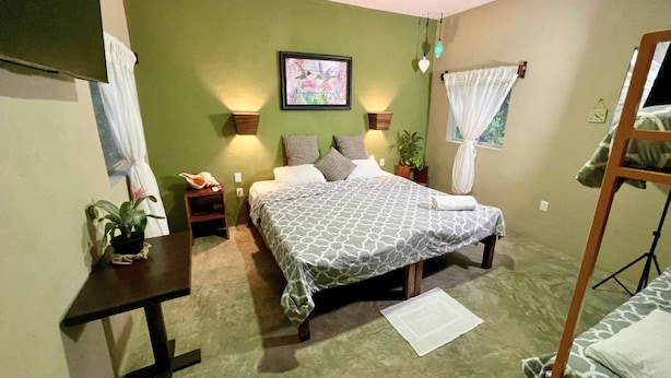 A bedroom with a bed, bedside tables, a desk, a chair, a bunk bed, a wall-mounted TV, and a framed picture. - #8 Tren Maya - Deluxe Family Room (Puerto Morelos)