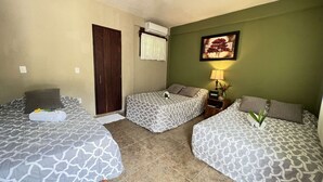 Une chambre d’hôtel avec deux lits simples, une armoire, un appareil de climatisation, une table de chevet avec une lampe et un tableau encadré au mur.