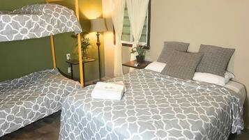 A room with two beds, a bedside table with a lamp, a potted plant, and a window with curtains.