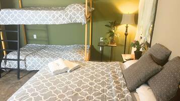 A dormitory room with bunk beds, a bedside table with a lamp, and a potted plant.