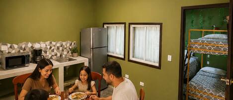Uma família jantando em uma cozinha compacta, com mesa, cadeiras e geladeira.