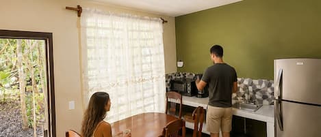 A compact kitchen with a dining area, a refrigerator, and a window with curtains.