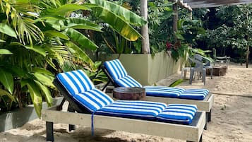 Un área de descanso junto a la playa con dos sillones a rayas y una mesita redonda.