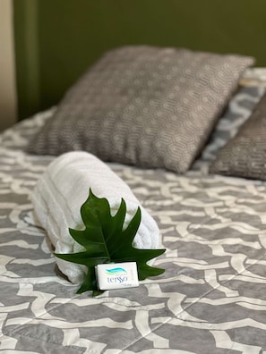 A neatly made bed with a patterned bedspread, a white towel, and a green leaf decoration.