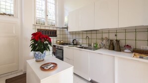 A kitchen with white cabinets, a stove, a sink, and a window with a view of greenery. - Popolo Square Luxury Two Bedroom Apartment (Roma)