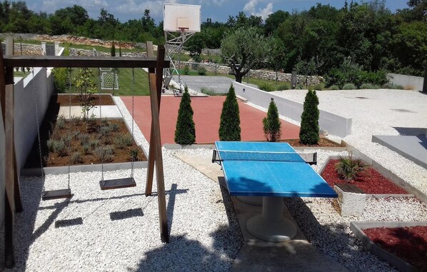 Uma quadra de tênis com superfície azul, rodeada por cascalho branco e cobertura de mulch vermelho.
