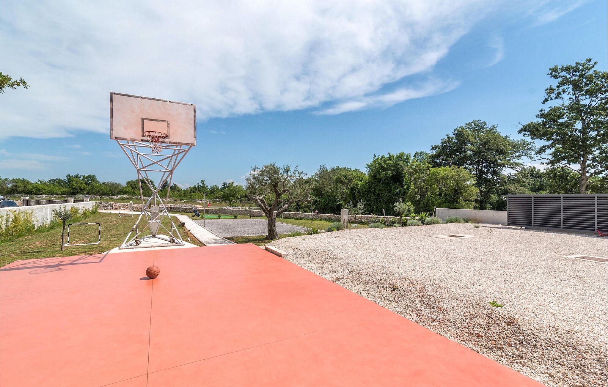 Una cancha de baloncesto al aire libre con superficie roja, aro de baloncesto y zona de grava.