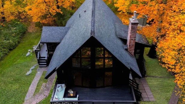 Uma cabana moderna com telhado triangular, rodeada por folhagem de outono.