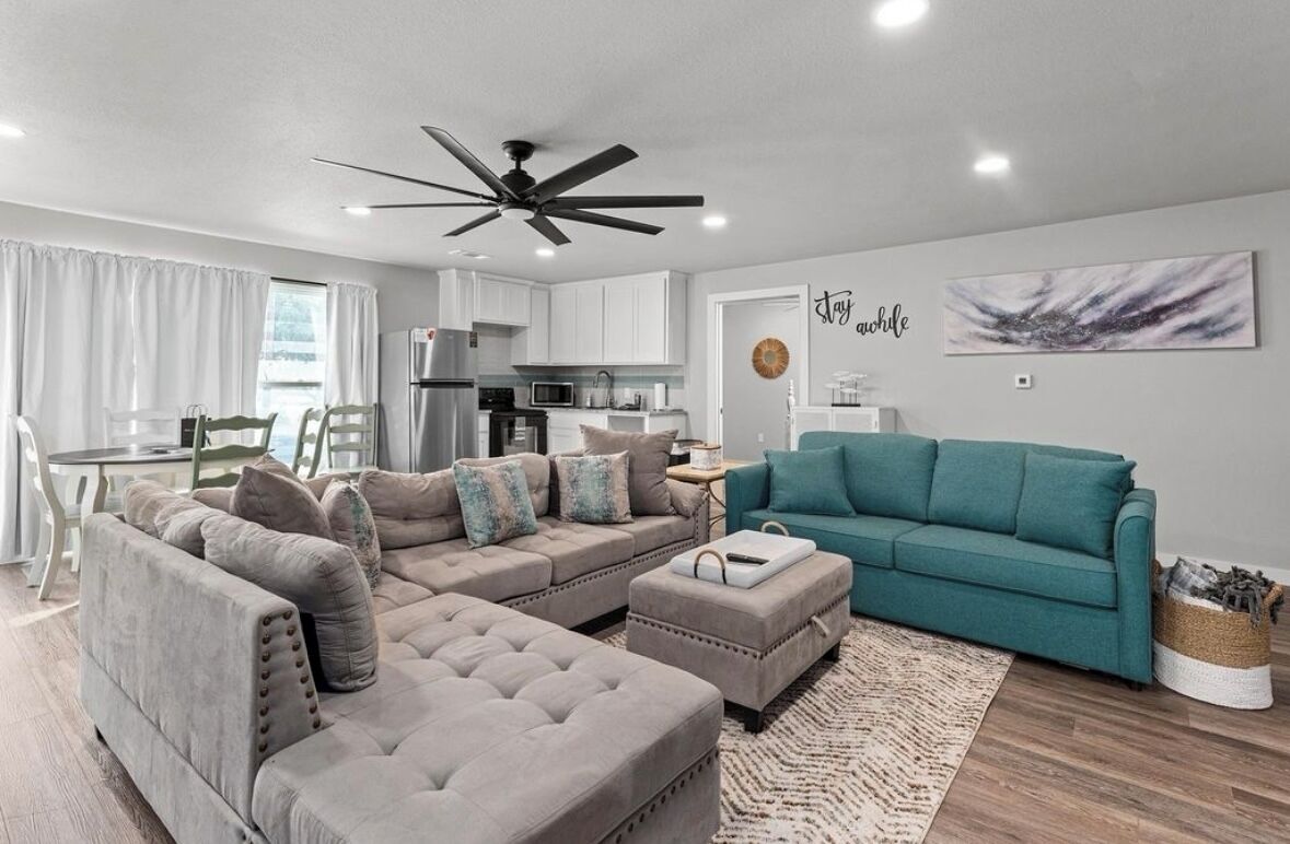 A modern living room with a sectional sofa, a teal couch, and a dining area with a table and chairs.