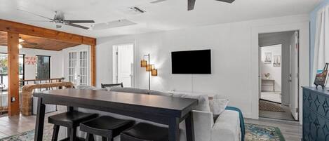 A modern living space with a dining area, a sofa, a TV mounted on the wall, and a ceiling fan.