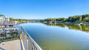 A riverfront view with a dock, a building with a balcony, and trees along the riverbank. - ParadiZe on Lake LBJ Open water 6 Bed 5 Bth Boat slip 2 jet ski ramps (Kingsland)