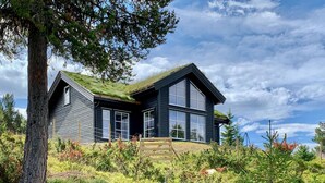 Ein zweistöckiges Haus mit steilem Satteldach, großen Fenstern und einer Holzterrasse.