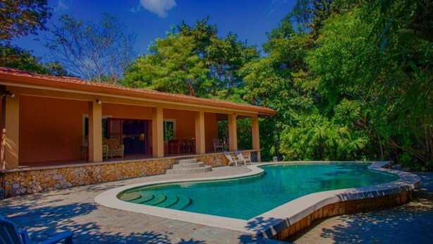 Une maison avec une piscine, des murs en pierre et un patio couvert avec des chaises.