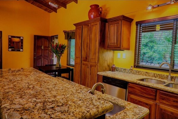 A kitchen with granite countertops, wooden cabinets, a large window with blinds, and a potted plant. - Henton Hacienda ,fiv minutes drive from the beach. (Los Pargos)