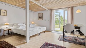Et moderne soveværelse med træloft, en seng med hvide sengetøj, et natbord med lampe, et skrivebord med stole og udsigt over det fri gennem et stort vindue.