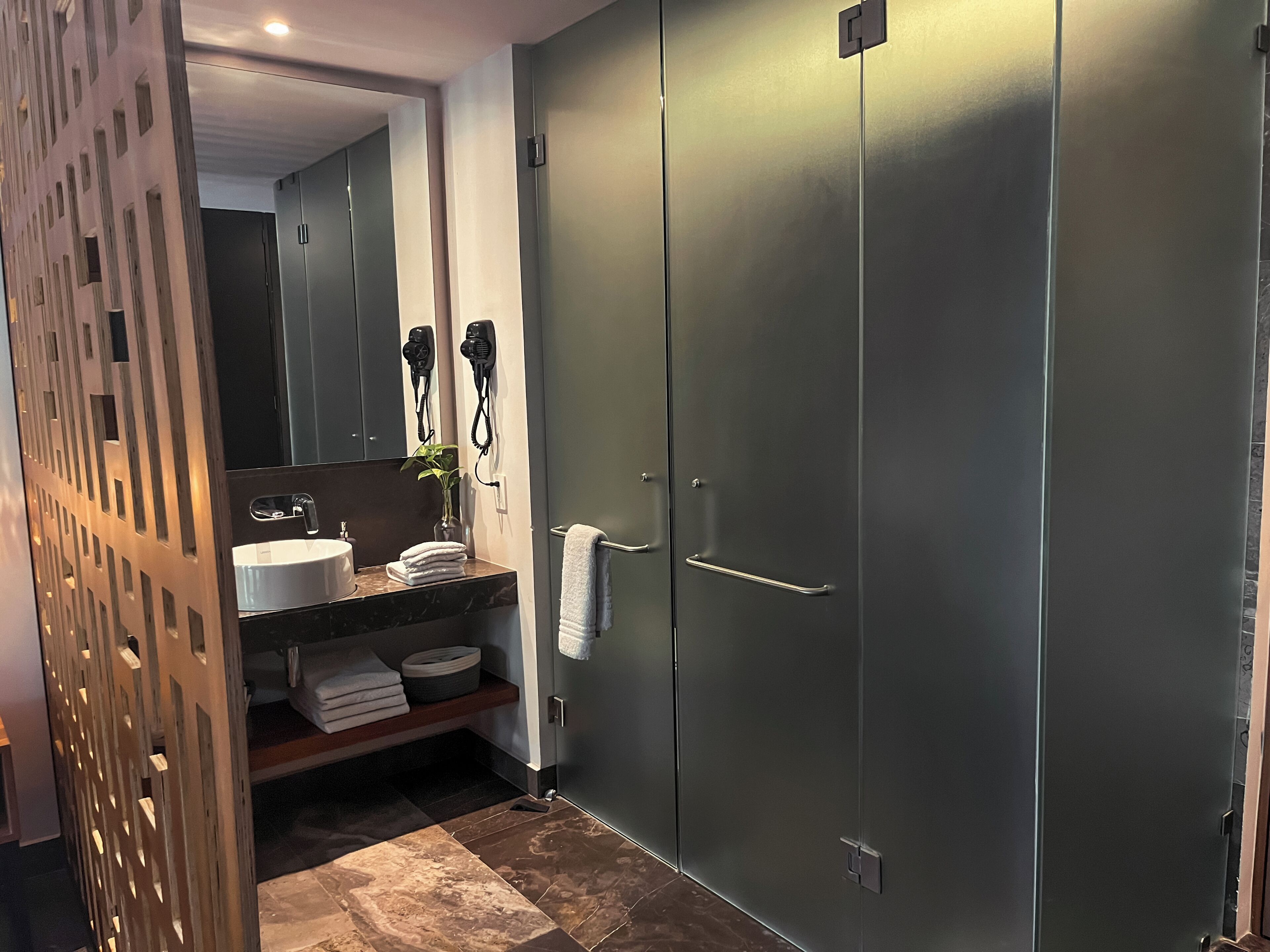A modern bathroom with a large mirror, a sink, and two hair dryers mounted on the wall.